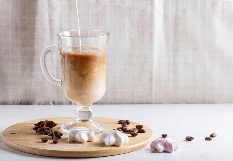 Glass cup of coffee with cream poured over and meringues on a wooden board on a white background. close up, copy space