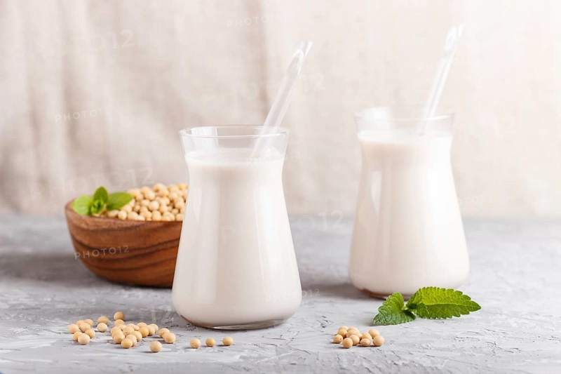 Organic non dairy soy milk in glass and wooden plate with soybeans on a gray concrete background. Vegan healthy food concept, close up, side view