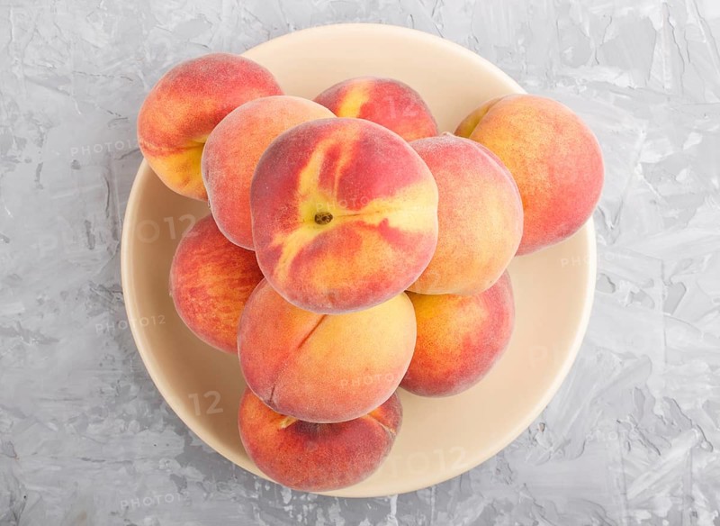 Fresh peaches on a plate on gray concrete background. top view, flat lay, close up