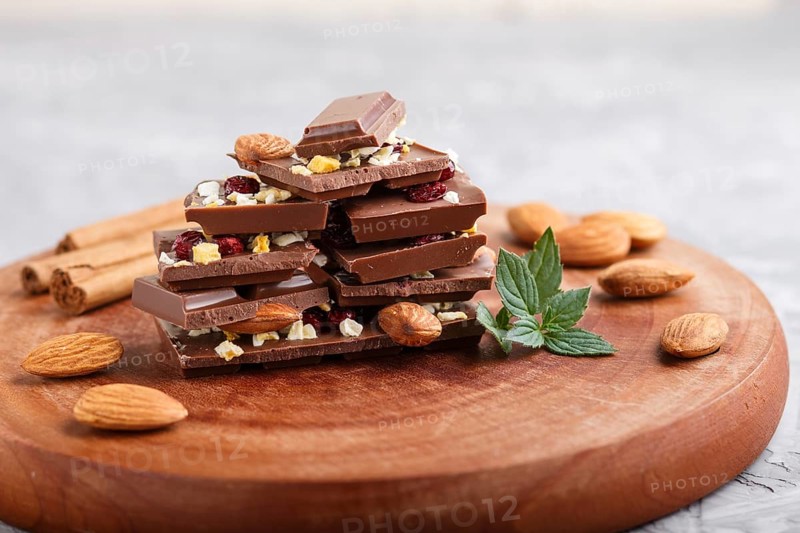 A pieces of milk chocolate with almonds and dried fruits on a brown wooden board on a gray concrete background. side view, close up, selective focus