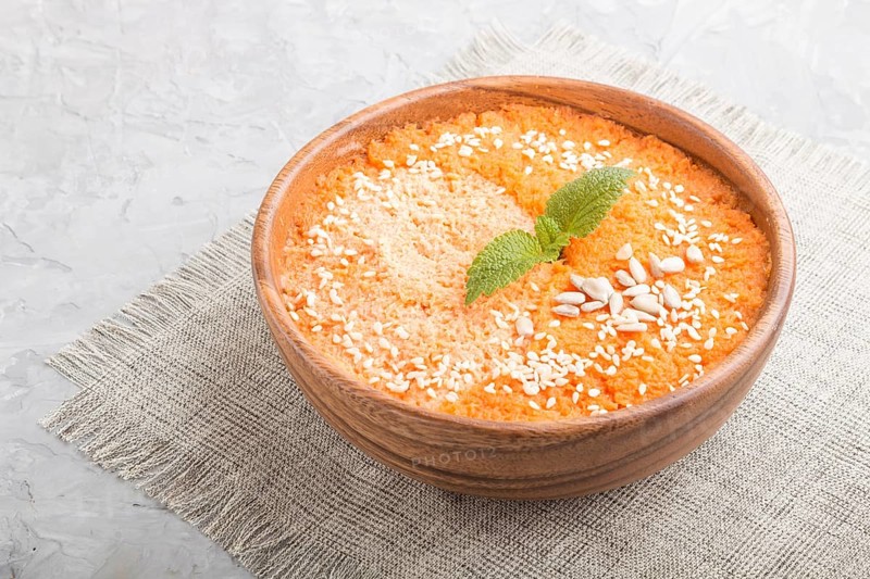 Carrot cream soup with sesame seeds in wooden bowl on a gray concrete background with linen textile. side view, close up