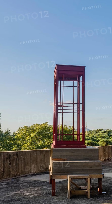 Red wooden telephone booth minus phone and without glass on roof of building on sunny day with blue skies in South Korea