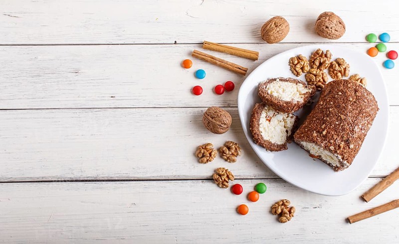 Roll cake with curd and walnuts isolated on white wooden background. top view, copy space