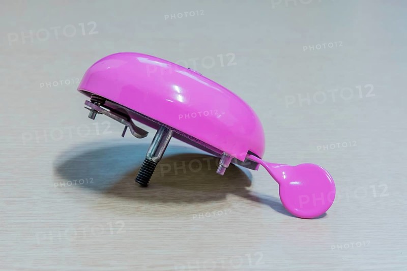 Pink handlebar bicycle bell with top missing isolated on light wood grain background