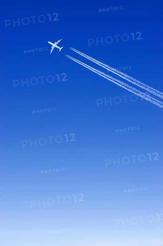 A passenger plane with vapour trails high in the blue sky