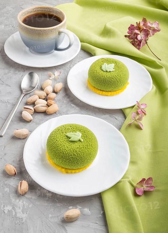 Green mousse cake with pistachio cream and a cup of coffee on a gray concrete background and green textile. side view, close up