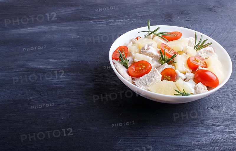 Chicken fillet salad with rosemary, pineapple and cherry tomatoes on dark blue wooden background. close up, copy space