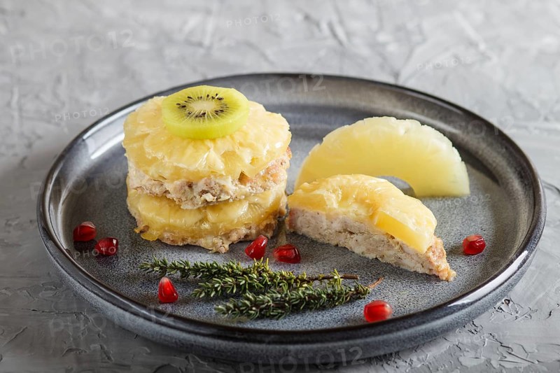 Pieces of baked pork with pineapple, cheese and kiwi on gray plate, side view, close up, selective focus