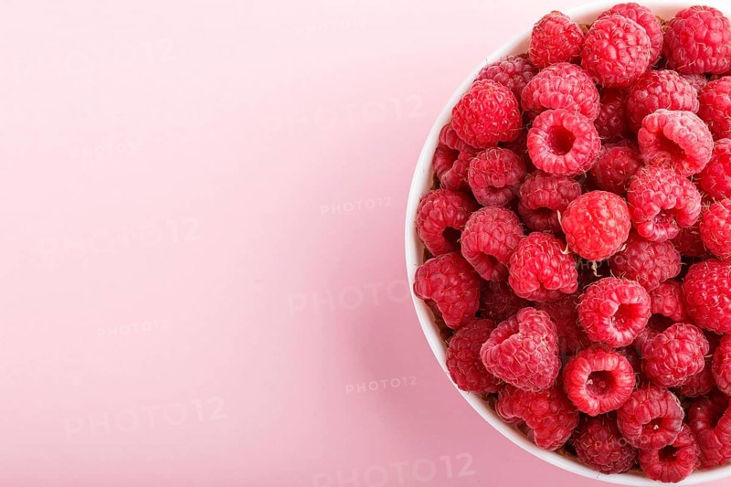 Fresh raspberry in white bowl on pink pastel background. top view, copy space, close up