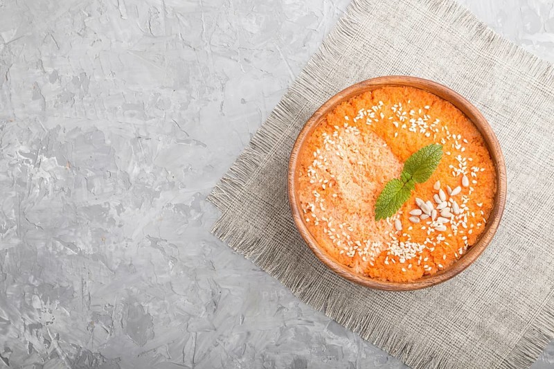 Carrot cream soup with sesame seeds in wooden bowl on a gray concrete background with linen textile. top view, flat lay, copy space