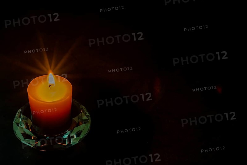 Burning candle in glass holder isolated on black textured background. Small amount of grain added for effect