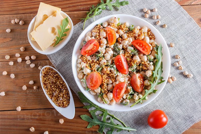 Vegetarian salad of boiled chickpeas, cheese, arugula, mustard and cherry tomatoes on brown wooden background. close up, top view