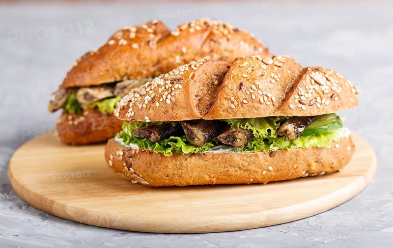 Sprats sandwiches with lettuce and cream cheese on wooden board on a gray concrete background. side view, close up