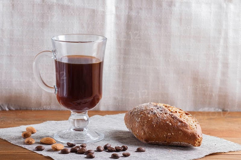 Glass cup of coffee with bun on a wooden background and linen textile. close up, copy space