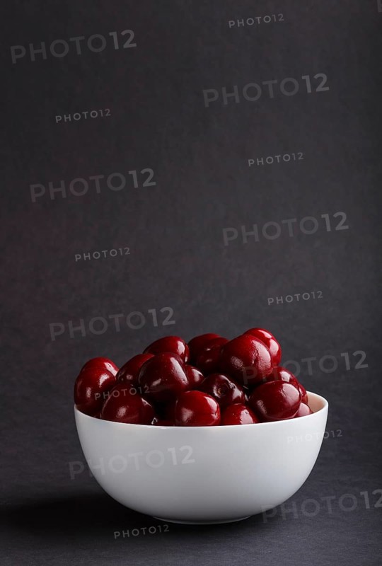 Fresh red sweet cherry in white bowl on black background. side view, copy space