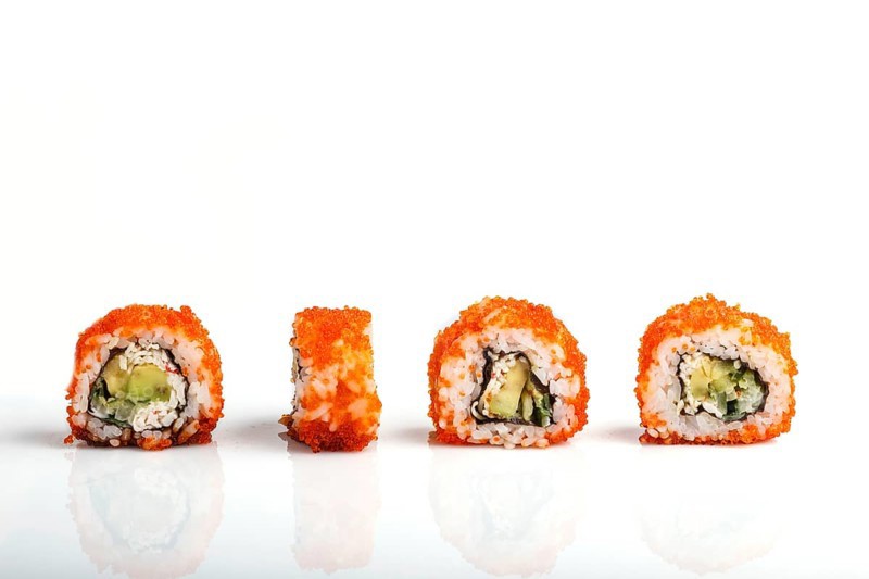 Four Japanese maki sushi rolls in a row with flying fish roe, avocado, and cucumber isolated on white background. Side view, close up