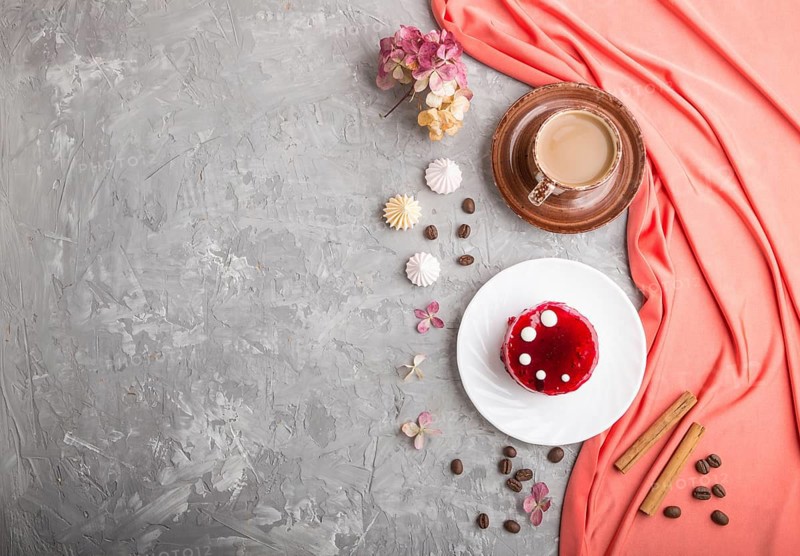 Red cake with souffle cream with cup of coffee on a gray concrete background and red textile. top view, flat lay, copy space