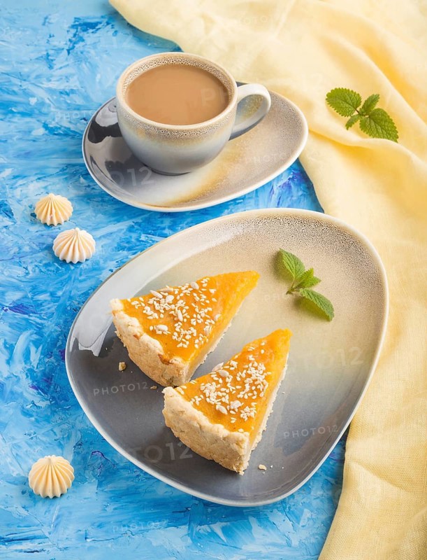 Two pieces of traditional american pumpkin pie with cup of coffee on a blue concrete background and yellow textile. side view, close up, contrast
