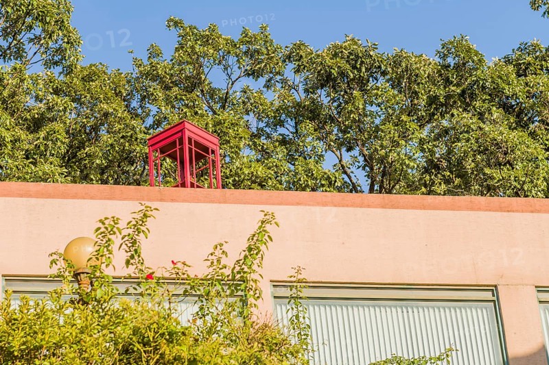 Red wooden telephone booth without glass on top of pink stucco building on sunny day with blue sky in South Korea