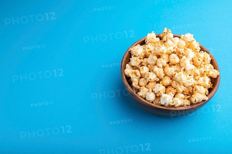 Popcorn with caramel in wooden bowl on a pastel blue background. Side view, copy space