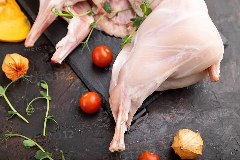Whole raw rabbit with pumpkin, tomatoes, pea sprouts on a black concrete background and linen textile. Side view, close up, selective focus