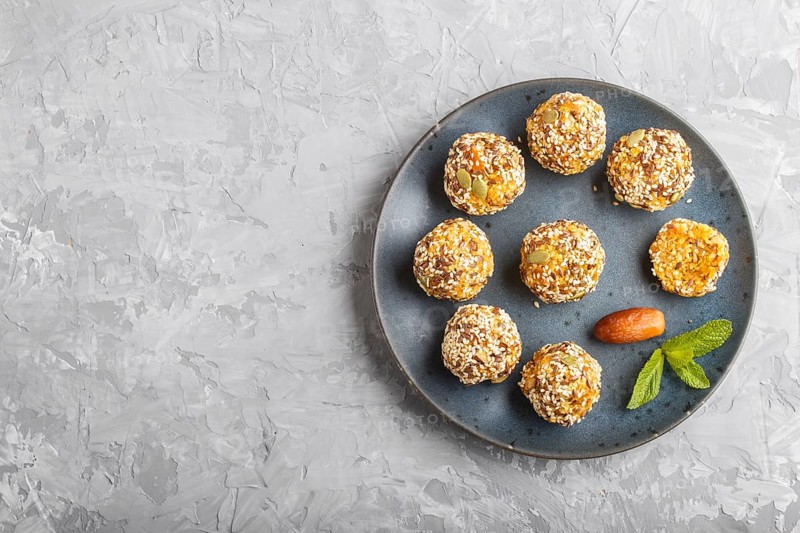 Energy ball cakes with dried apricots, sesame, linen, walnuts and dates with green mint leaves on a blue ceramic plate on a gray concrete background. top view, copy space, flat lay. vegan homemade candy