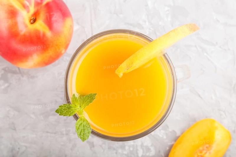 Glass of peach juice on a gray concrete background. Morninig, spring, healthy drink concept. Top view, close up, flat lay