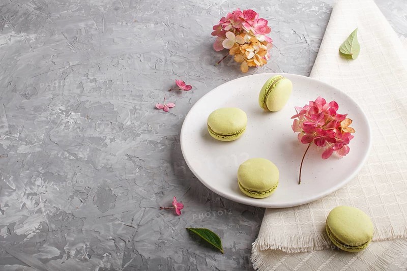 Green macarons or macaroons cakes on white ceramic plate on a gray concrete background and linen textile. side view, copy space