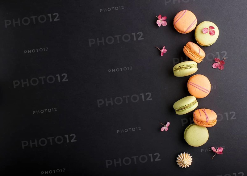 Orange and green macarons or macaroons cakes on black background. top view, flat lay, copy space
