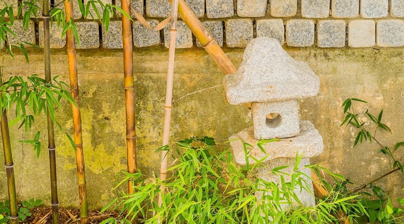 Small cement spirit house in front of concrete wall next to young bamboo plants in South Korea