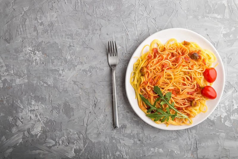 Corn noodles with tomato sauce and arugula on a gray concrete background. Top view, flat lay, copy space