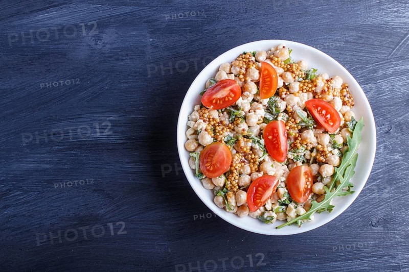 Vegetarian salad of boiled chickpeas, cheese, arugula, mustard and cherry tomatoes on black wooden background. copy space, top view