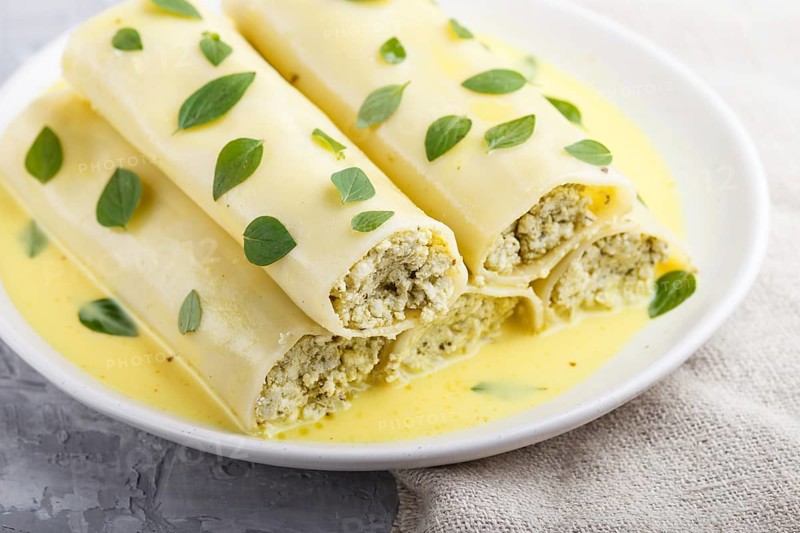 Cannelloni pasta with egg sauce, cream cheese and oregano leaves on a gray concrete background with linen textile. side view, close up, selective focus
