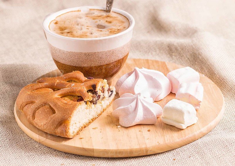 Sweet buns, meringues and coffee cup on a wooden board and linen tablecloth