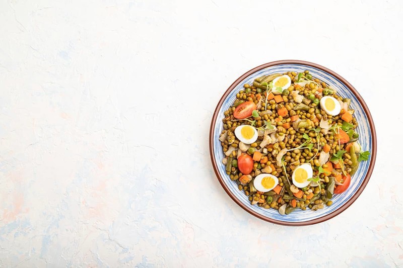 Mung bean porridge with quail eggs, tomatoes and microgreen sprouts on a white concrete background. Top view, flat lay, copy space