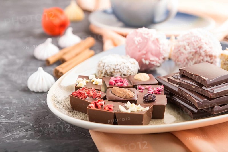 A pieces of homemade chocolate with coconut candies and a cup of coffee on a black concrete background and orange textile. side view, close up, selective focus