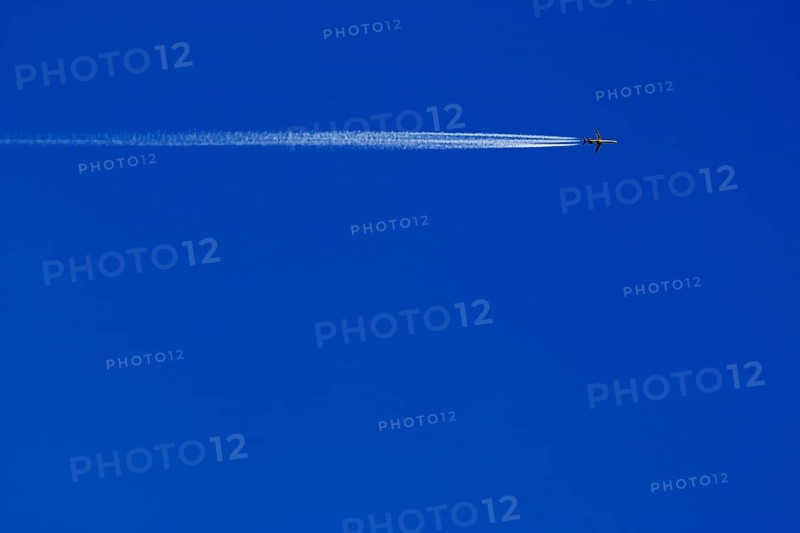 A passenger plane with vapour trail high in the blue sky