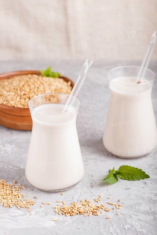 Organic non dairy oats chocolate milk in glass and wooden plate with oats seeds on a black concrete background. Vegan healthy food concept, close up, side view