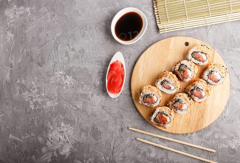 Japanese maki sushi rolls with salmon, sesame, chopsticks, soy sauce and marinated ginger on wooden board on a gray concrete background. Top view, copy space