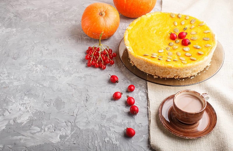 Traditional american sweet pumpkin pie decorated with hawthorn red berries and pumpkin seeds with cup of coffee on a gray concrete background. side view, copy space