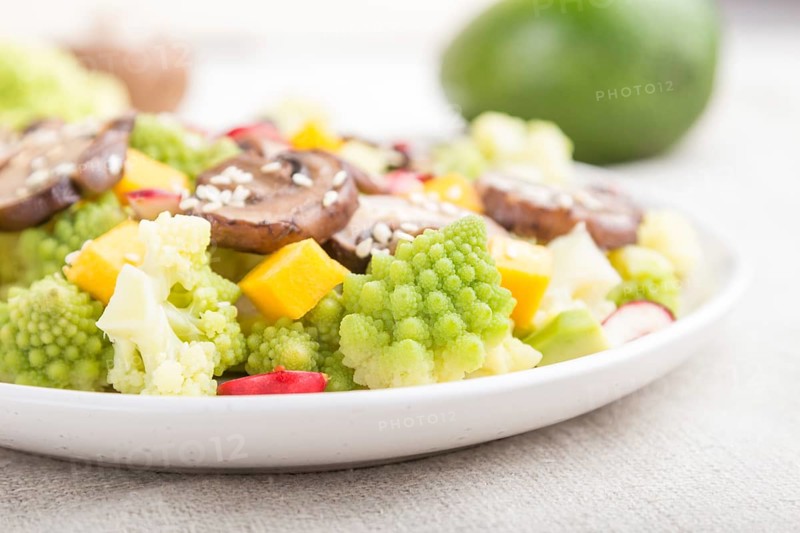Vegetarian salad from romanesco cabbage, champignons, cranberry, avocado and pumpkin on a white wooden background and linen textile. side view, close up, selective focus