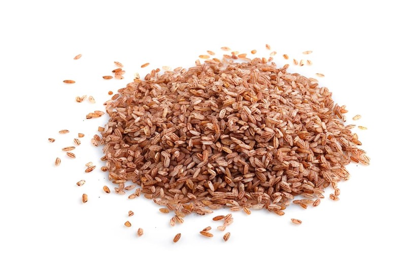 Heap of unpolished brown rice isolated on white background. Side view, flat lay, close up, macro