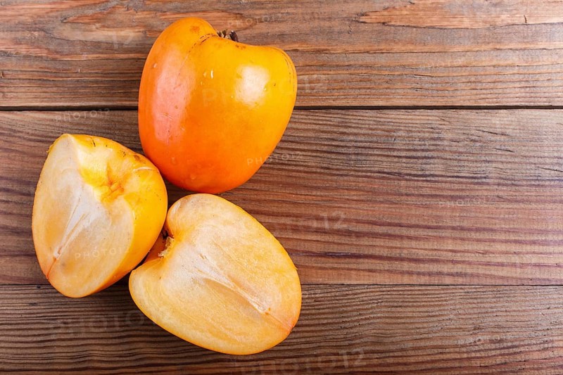 Ripe orange persimmon on brown wooden background, with copy space, top view