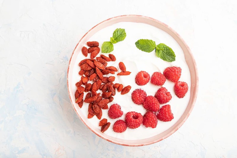 Yogurt with raspberry and goji berries in ceramic bowl on white concrete background. top view, flat lay, close up