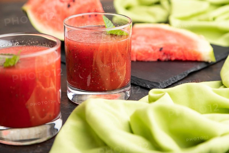 Watermelon juice with chia seeds and mint in glass on a black concrete background with green textile. Healthy drink concept. Side view, close up, selective focus