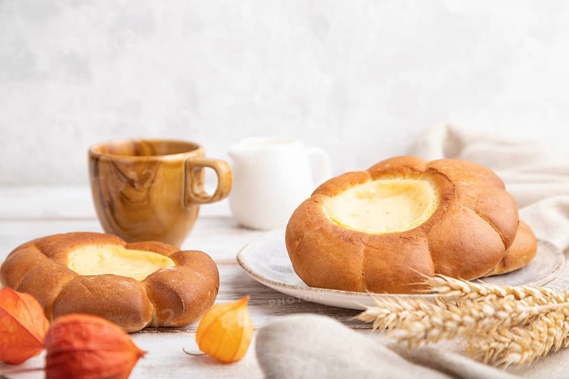 Sour cream bun with cup of coffee on a white wooden and concrete background and linen textile. Side view, close up, selective focus