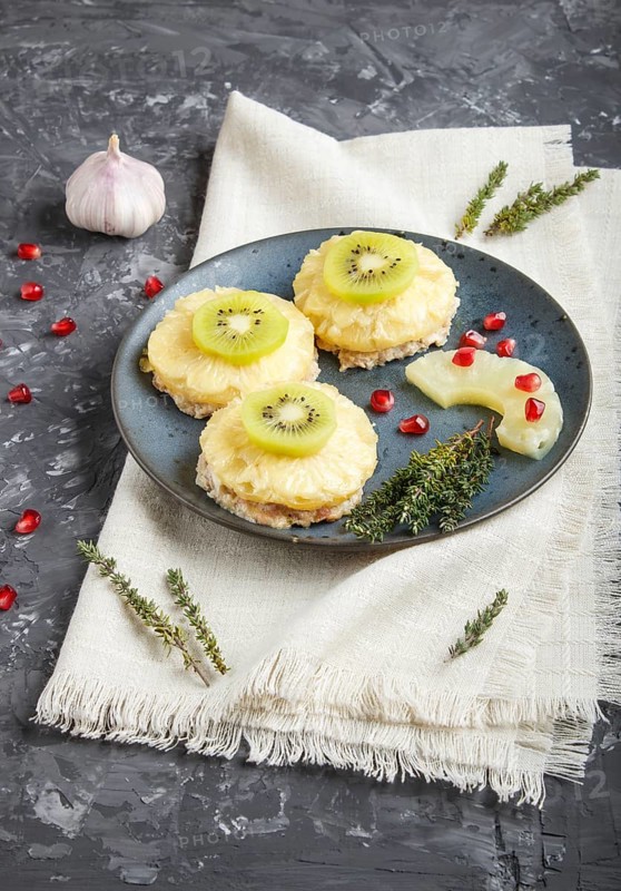 Pieces of baked pork with pineapple, cheese and kiwi on black background, side view, close up