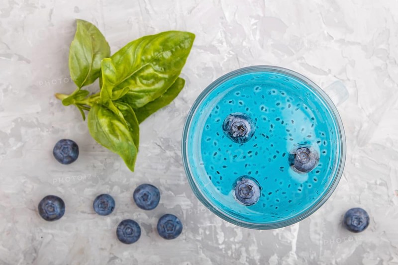 Glass of blueberry blue colored drink with basil seeds on a gray concrete background. Morninig, spring, healthy drink concept. Top view, close up, flat lay