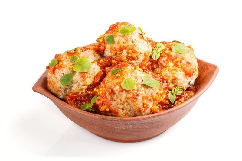 Pork meatballs with tomato sauce, oregano leaves, spices and herbs in clay bowl isolated on white background. side view, close up