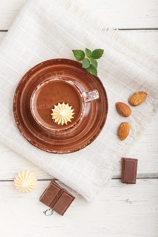 Cup of hot chocolate and pieces of milk chocolate with almonds on a white wooden background with linen napkin. top view, flat lay, close up